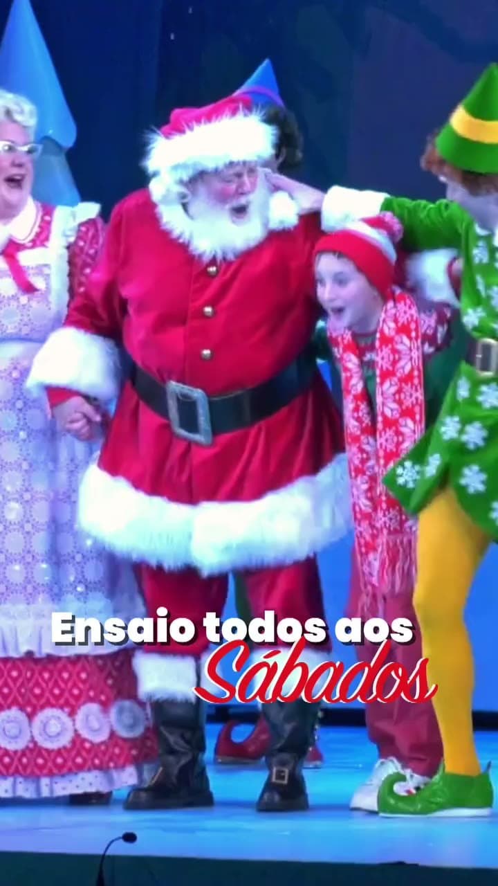 Papai Noel, Mamãe Noel e um duende em cena com uma criança, no palco do espetáculo da Sede