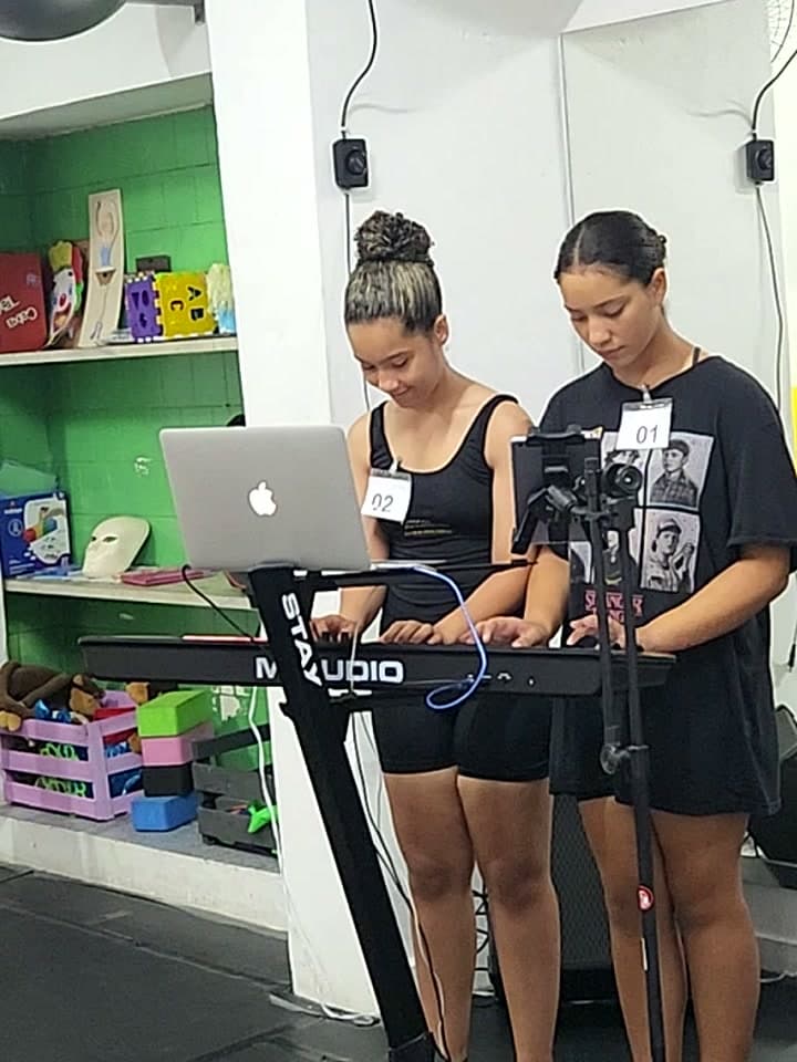 Duas candidatas ao teclado e ao microfone, com os números 01 e 02 na roupa, durante a avaliação de música