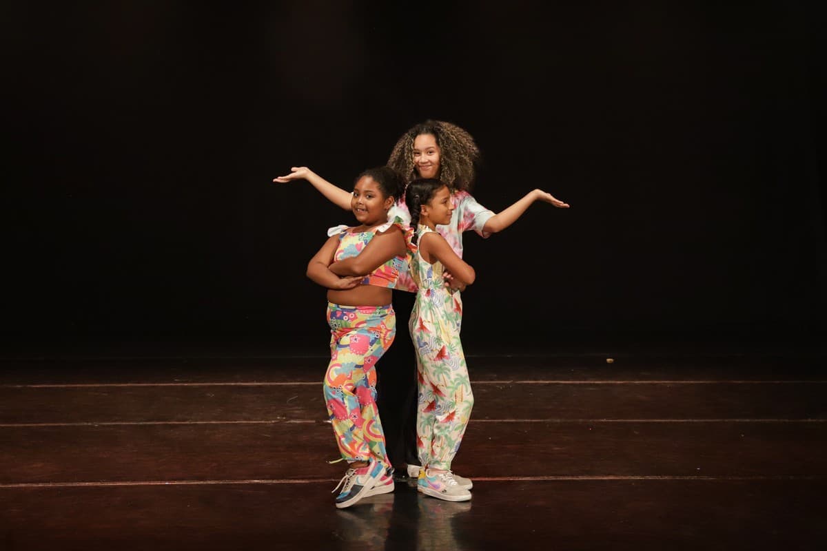 Três alunas de roupas estampadas posando no palco